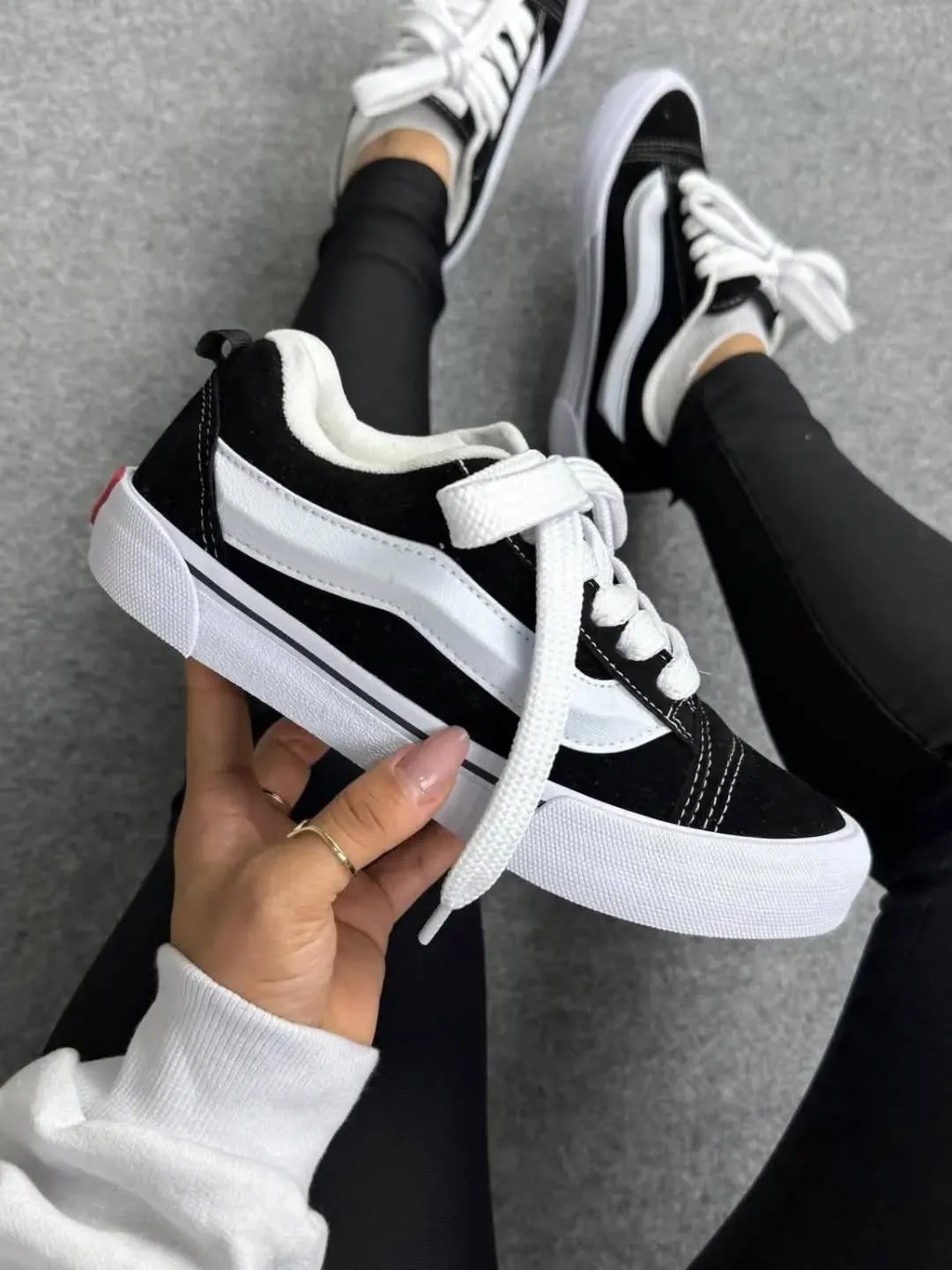 Vans Knu Skool preto e branco na mão, no chão de concreto